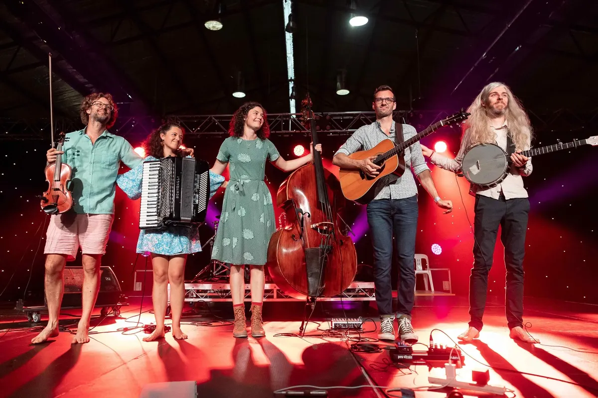 The five members of The Good Behaviours taking a bow on a stage washed in red light, instruments in hand